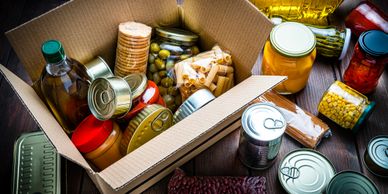 box of non-perishable food items in it; some non-perishable food items on table