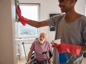 Woman cleaning cupboard while man in wheelchair watches on