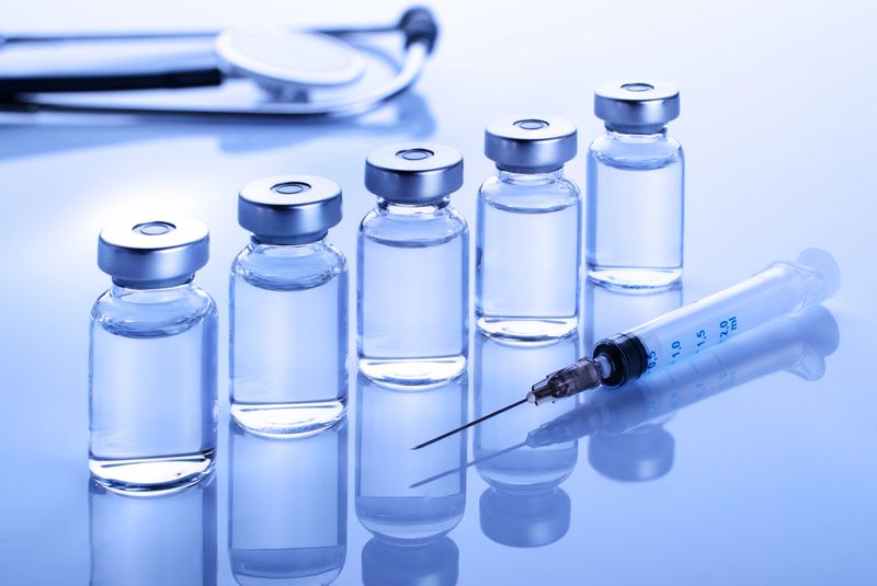 Vials with liquid drug as vaccine dose flu shot along with stethoscope, syringe for injection treatment on medical table. Vaccination or immunization care concept background.
