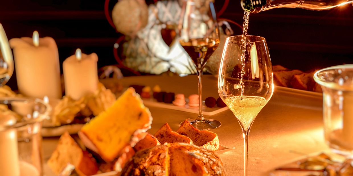 Wine being poured into a glass on a candlelit table with bread and desserts.