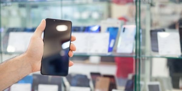 Hand holding a smartphone in front of a glass display case with phones.