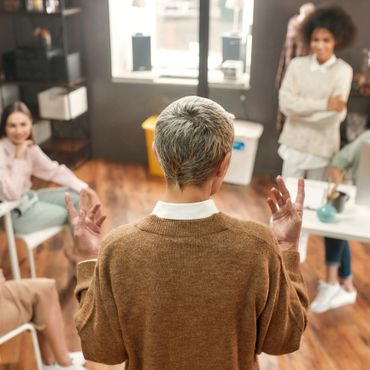 Person speaking to a small group in a cozy room with wooden floors.