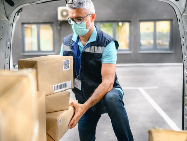 Delivery worker loading packages into a vehicle wearing a mask.