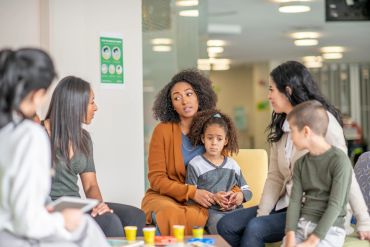 Group therapy session with diverse adults and children in a supportive environment.