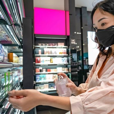 Woman testing perfume spray in a store while wearing a mask.