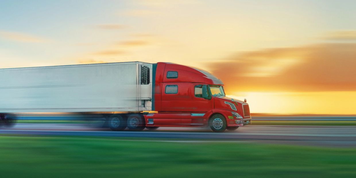 A red semi-truck speeding on a highway during sunset.