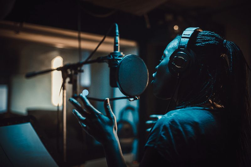 One woman, beautiful black female vocalist wearing headphones and singing into microphone in recording studio.