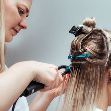 Hair stylist applying hair extensions with tools and clips.