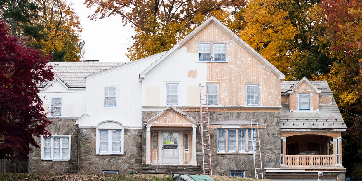A house partially painted white with ladders set up outside.