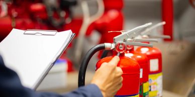 Person inspecting fire extinguisher with clipboard.