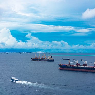 Cargo ships and a small boat on a blue ocean under a cloudy sky.