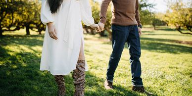 Couple holding hands walking through a sunlit orchard.