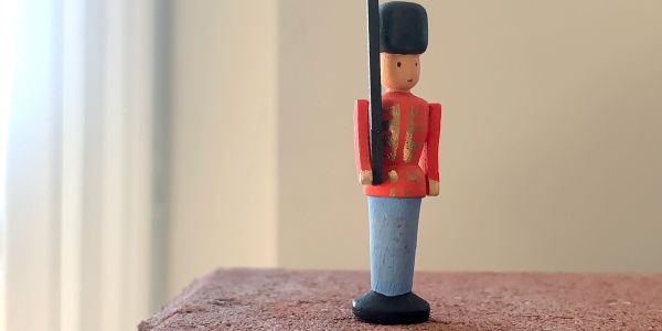 Wooden toy soldier standing on a brick surface indoors.