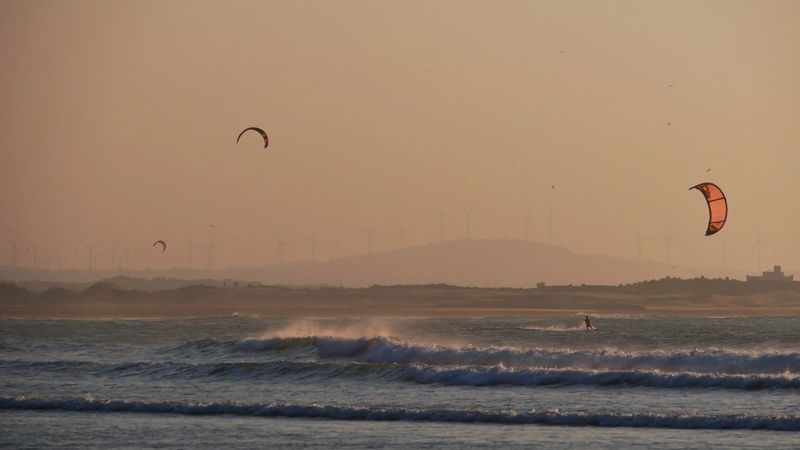 Kite surfers with colorful kites enjoying to ride the waves on the beach of Essaouira, Morocco, Africa in the wild Atlantic Ocean on a winter day with hazy air.
