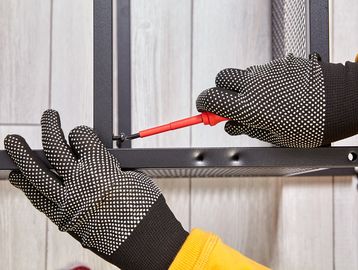 Hands in gloves assembling furniture with a screwdriver.