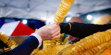 Person buying a twisted fried potato snack on a stick.