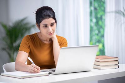 Young woman studying with laptop and notebook at a desk.