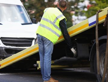 Worker loading a damaged car onto a tow truck.