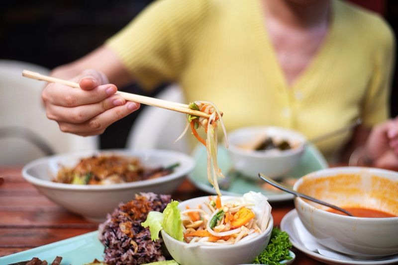 Woman having Som Tam green papaya salad classical Thai food of with BBQ chicken, sticky rice and raw salad vegetables on a wooden table background