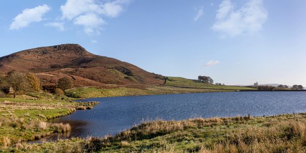 Calm lake with grassy banks and a hill under a clear blue sky.
