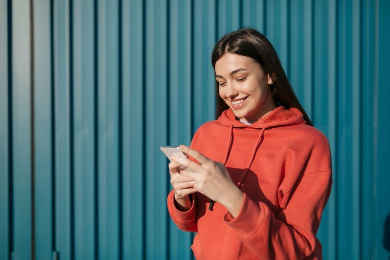 Beautiful young happy Caucasian woman standing outdoors, having fun, smiling and using a smart phone