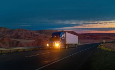 A truck driving on a highway at dusk with mountains in the background.