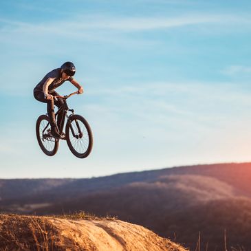 A cyclist performs a high jump on a mountain bike against a clear sky.