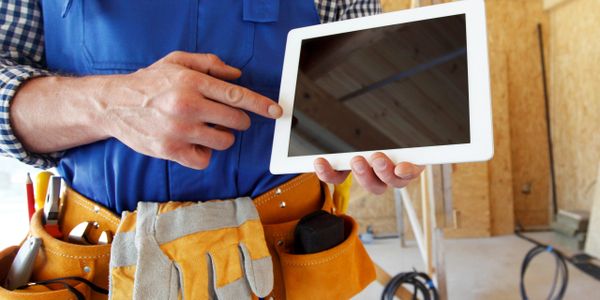 Construction worker holding and pointing at a tablet in a building site.