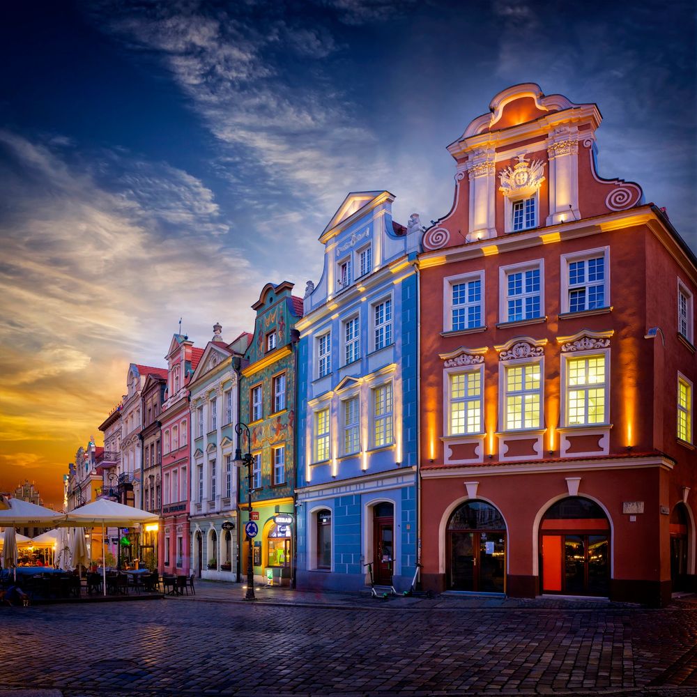 Colorful historic buildings lit up at sunset with outdoor dining on a cobblestone street.