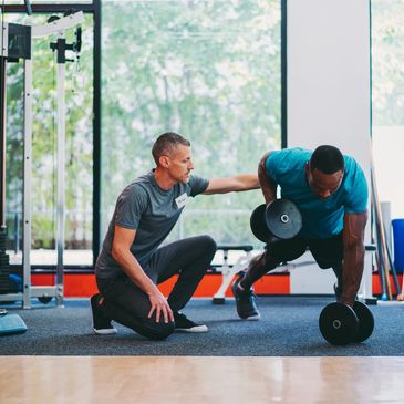 Personal trainer coaching a man doing dumbbell rows in a gym.