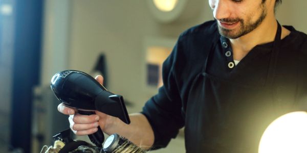 Barber using a hairdryer and brush to style a client's hair.