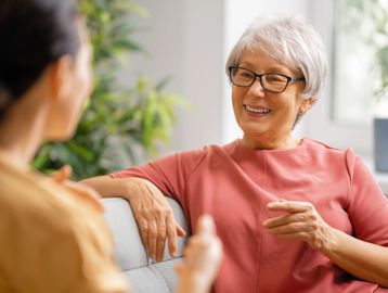 An elderly woman sitting on a couch, mid-conversation with a young woman.