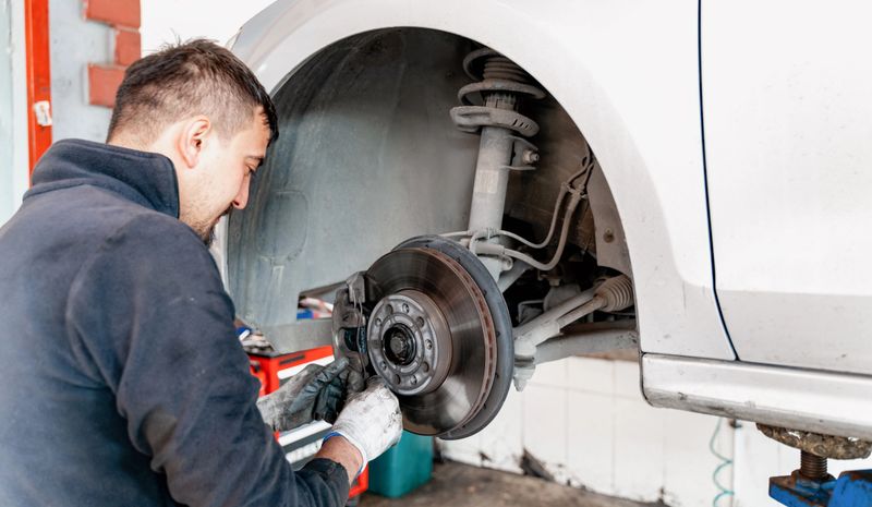 Car mechanic hands replace brakes in garage. Mechanic technician worker installing car wheel at maintenance. Worker changing brake disc. Brake disc installation concept. - can use to display or montage product or make a website for service