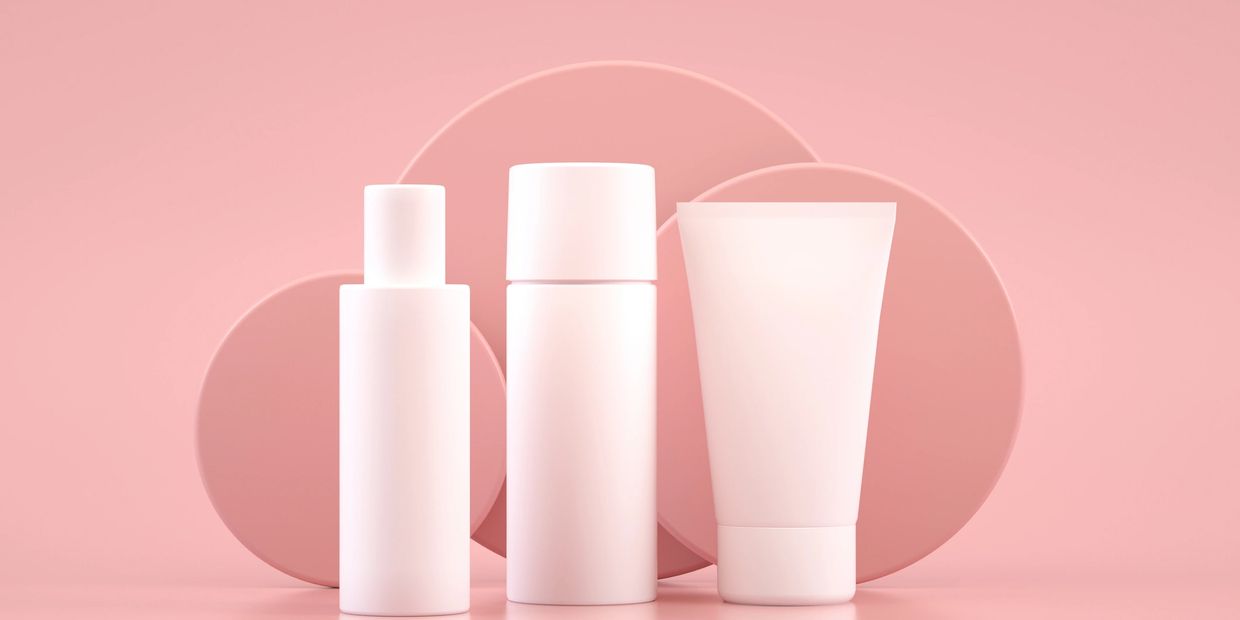 Three white cosmetic bottles on pink background.