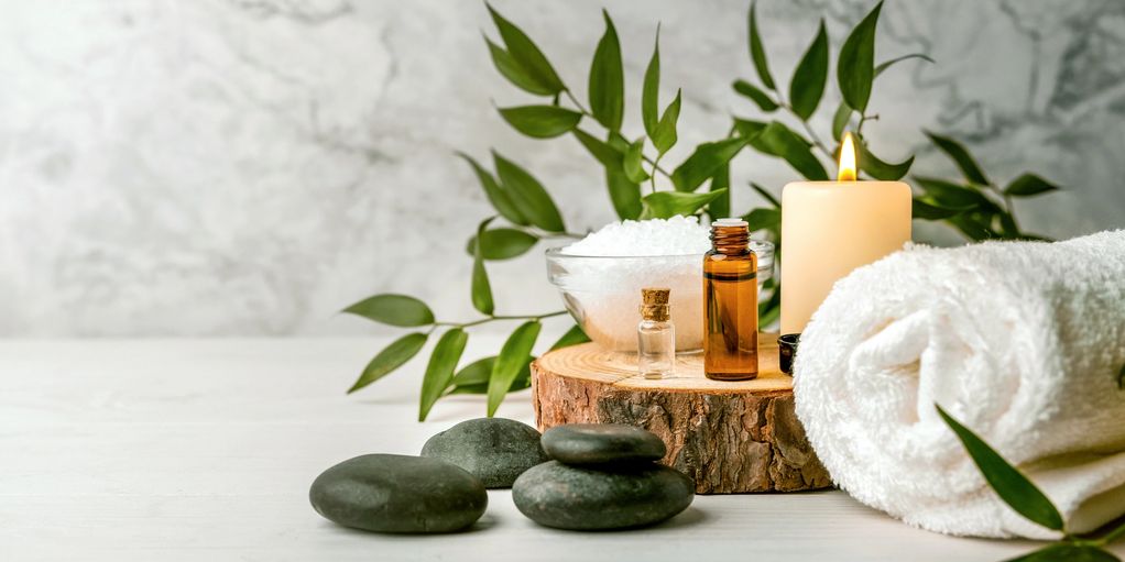 Spa setup with stones, towel, candle, essential oils, and greenery.