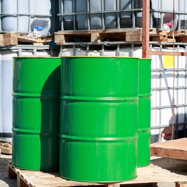 Three green metal barrels placed on a wooden pallet outdoors.
