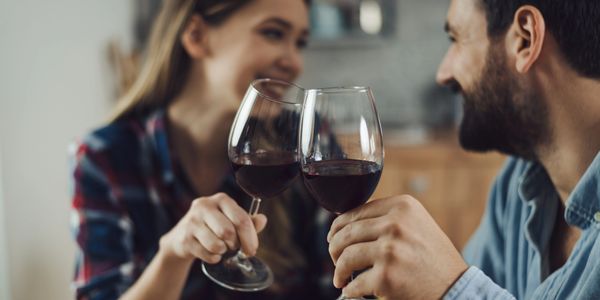 a man and a women smiling at eachother while holding red wine glasses