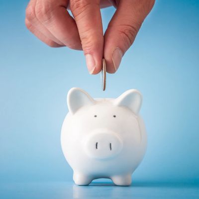 Hand putting coin into white piggy bank.