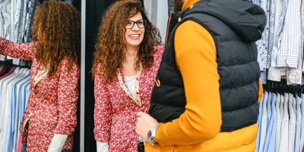 Woman smiling while trying on a red floral jacket in front of a mirror.