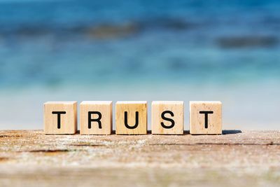 Wooden blocks spelling the word TRUST on a beach background.