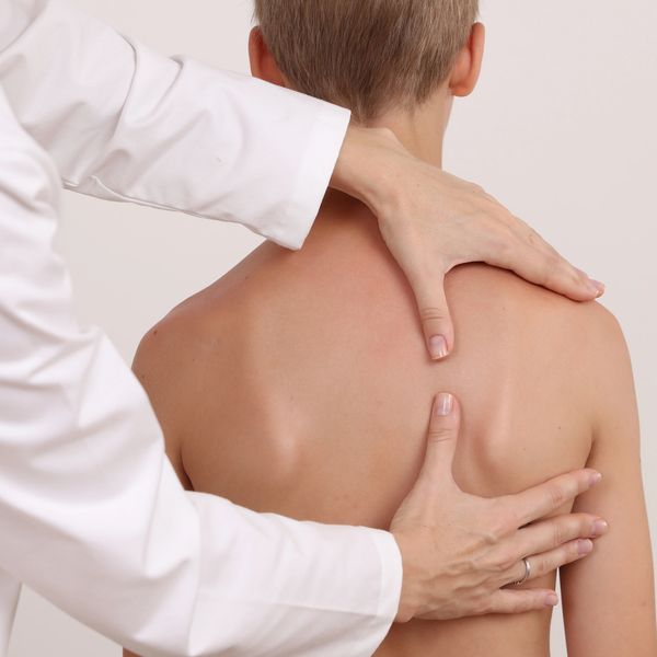 Doctor examining a boy's back, checking for posture or spine issues.