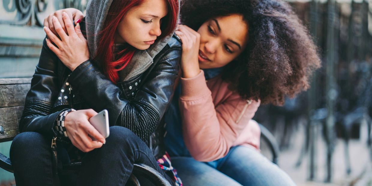 One woman comforts another who looks upset on a bench.