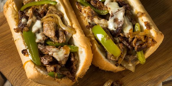 Two Philly cheesesteak sandwiches with melted cheese and green peppers on a wooden board.