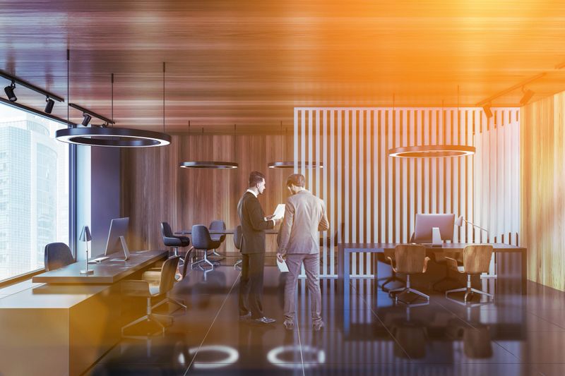 Portrait of two businessmen standing in CEO office with wooden and gray walls, gray floor and meeting room in background. Toned image