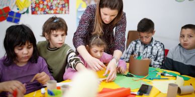Teacher helping children with crafts in a colorful classroom.