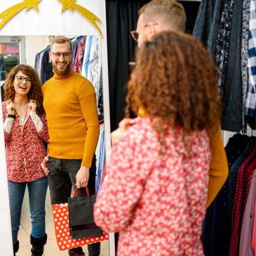 Couple happily trying on clothes in a store mirror.