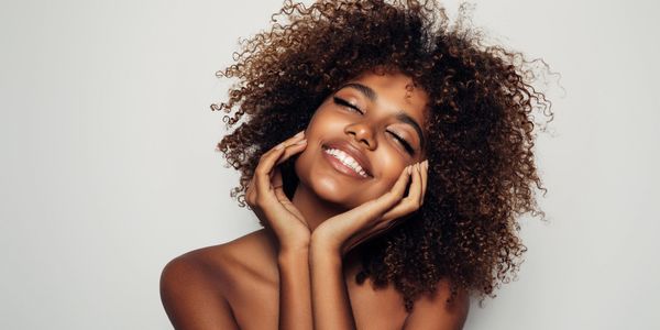 Smiling woman with curly hair and glowing skin.