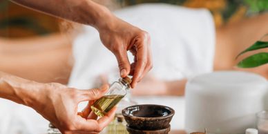 Hands holding essential oil bottle near aroma diffuser and crystals on wooden table.