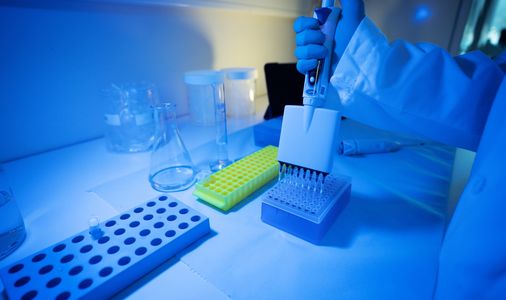 Scientist using a multi-channel pipette in a blue-lit laboratory.