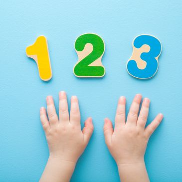 Baby's hands with colorful wooden numbers 1, 2, and 3 on blue background.
